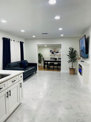 A modern kitchen with white cabinets, a dining area with a black table and chairs, and a living area with a black sofa. - A Cozy Getaway Just 3 Minutes from the Casino (Tampa)