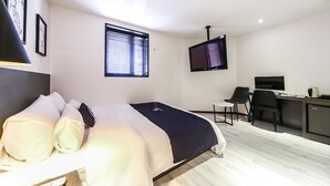 A modern bedroom with a bed, a desk, a chair, a TV, and a window with blinds.