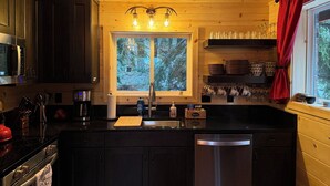 Una cocina con armarios de madera, un refrigerador de acero inoxidable, un microondas y una ventana con vista a árboles.