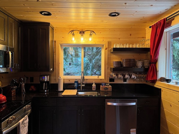 Una cocina con armarios de madera, un refrigerador de acero inoxidable, un microondas y una ventana con vista a árboles.