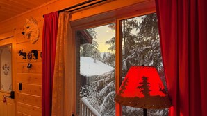 Una habitación con paredes de madera, una ventana con cortinas rojas, una cabeza de animal colgada en la pared y una lámpara roja.