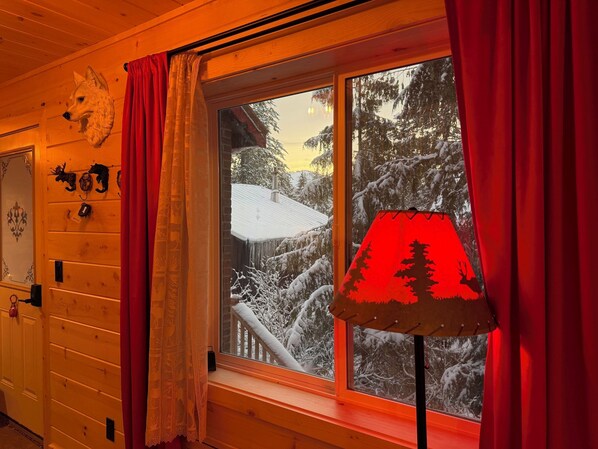 Una habitación con paredes de madera, una ventana con cortinas rojas, una cabeza de animal colgada en la pared y una lámpara roja.