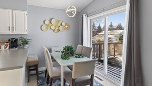 A modern kitchen with white cabinets, a coffee maker, and a dining area with a table, chairs, and a plant. - Delightful 5-bedroom house with AC in Little Canada (Little Canada)