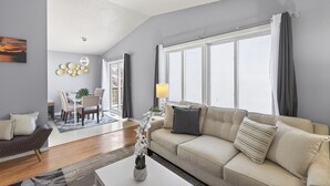 A modern living room with a sofa, a coffee table, and a dining area with a table and chairs. - Delightful 5-bedroom house with AC in Little Canada (Little Canada)