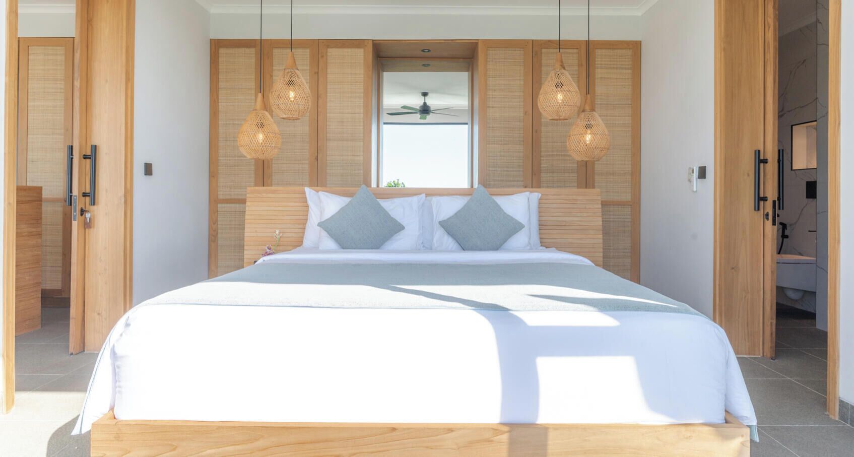 Ein modernes Schlafzimmer mit einem großen Bett, einem Holz-Kopfteil und zwei Pendelleuchten.