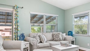 A living room with a beige sofa, white coffee table, and a patterned curtain. - Walk to beach & trail-bikes, beach gear, porch (Palm Harbor)