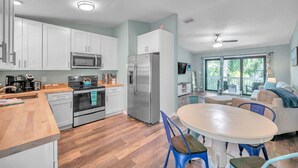 A modern kitchen with white cabinets, stainless steel appliances, and a wooden countertop. There is a dining area with a round table and blue chairs. - Bike to trails, beach, parks - great for families! (Palm Harbor)