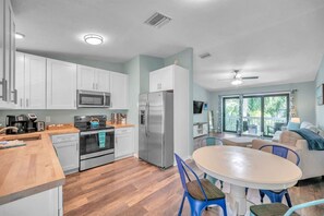 A modern kitchen with white cabinets, stainless steel appliances, and a wooden countertop. There is a dining area with a round table and blue chairs. - Bike to trails, beach, parks - great for families! (Palm Harbor)