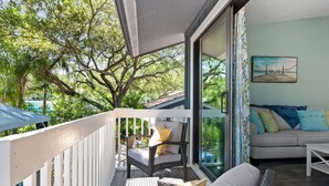 A balcony with a wicker chair and cushions, a white railing, and a view of trees and a building. - Bike to trails, beach, parks - great for families! (Palm Harbor)