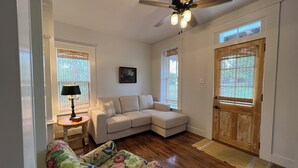 A living room with a beige sectional sofa, a floral armchair, a wooden floor, a ceiling fan, and a door with a window. - Restored 2-bedroom cottage in beautiful California, MO (California)