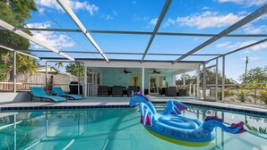 Una piscina con juguetes inflables, sillas de descanso y una zona de estar cubierta.