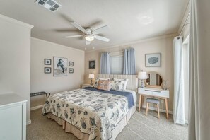 Ein Schlafzimmer mit Bett, Nachttischen, Schreibtisch, Stuhl, Deckenventilator und Wandbildern.
