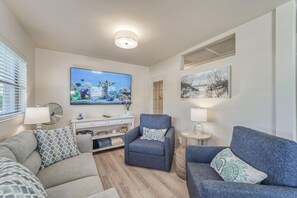 Un salon moderne avec un téléviseur à écran plat, deux canapés, un fauteuil bleu et une petite table d’appoint.