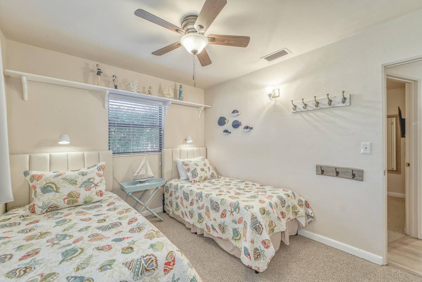 Une chambre avec deux lits, un ventilateur de plafond, une fenêtre avec des stores et des éléments de décoration fixés au mur.