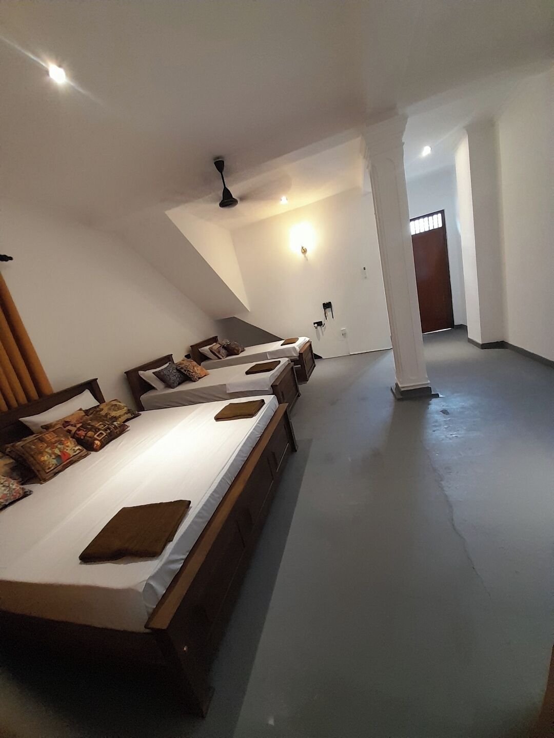 Una habitación de hotel con tres camas individuales, un ventilador de techo y una lámpara en la pared.