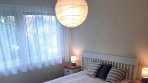Une chambre à coucher bien aménagée, avec un grand lit, deux tables de chevet avec des lampes, un luminaire suspendu et un tapis à rayures.