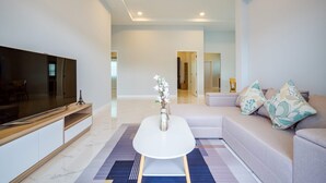 Una sala de estar moderna con un televisor de pantalla plana, una mesa de centro blanca, un sofá beige y cojines estampados.