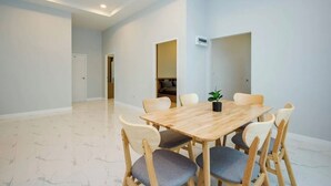 Una habitación amplia con una mesa de comedor de madera y sillas, una planta en maceta y un equipo de aire acondicionado blanco en la pared.