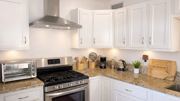 Una cocina moderna con armarios blancos, extractor de acero inoxidable, horno empotrado, tostadora y diversos utensilios de cocina.