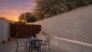 Un patio trasero con muro de ladrillo, valla de madera y una mesa con sillas.