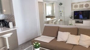 Un salon moderne avec un canapé beige, une table basse en verre et un téléviseur fixé au mur.