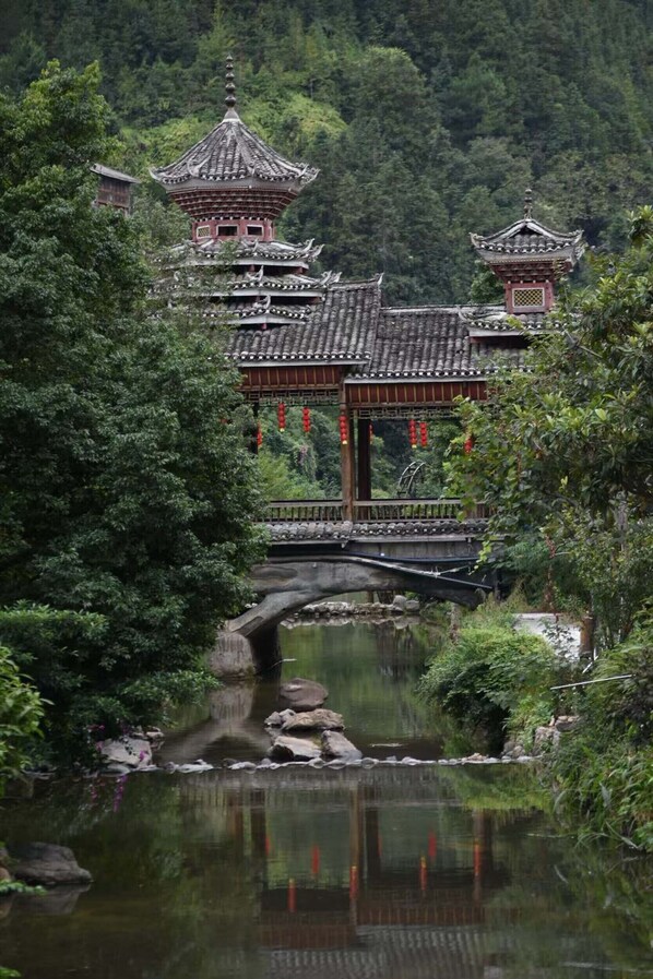 A traditional Chinese pavilion with a tiled roof, surrounded by lush greenery and a calm pond. - Drum Tower Sightseeing B&B. (Qiandongnan)