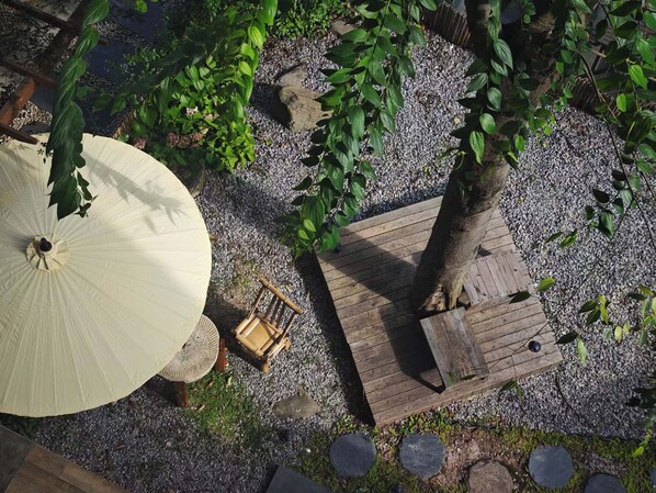 Una terraza de madera con una mesa y sillas, rodeada de grava y follaje.