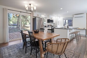 A modern kitchen with a wooden dining table, black chairs, and a large island with stools. - Woodhaven House- 1-Acre Bend Oasis, Hot tub, w/office Studio, Pet-Friendly (Bend)