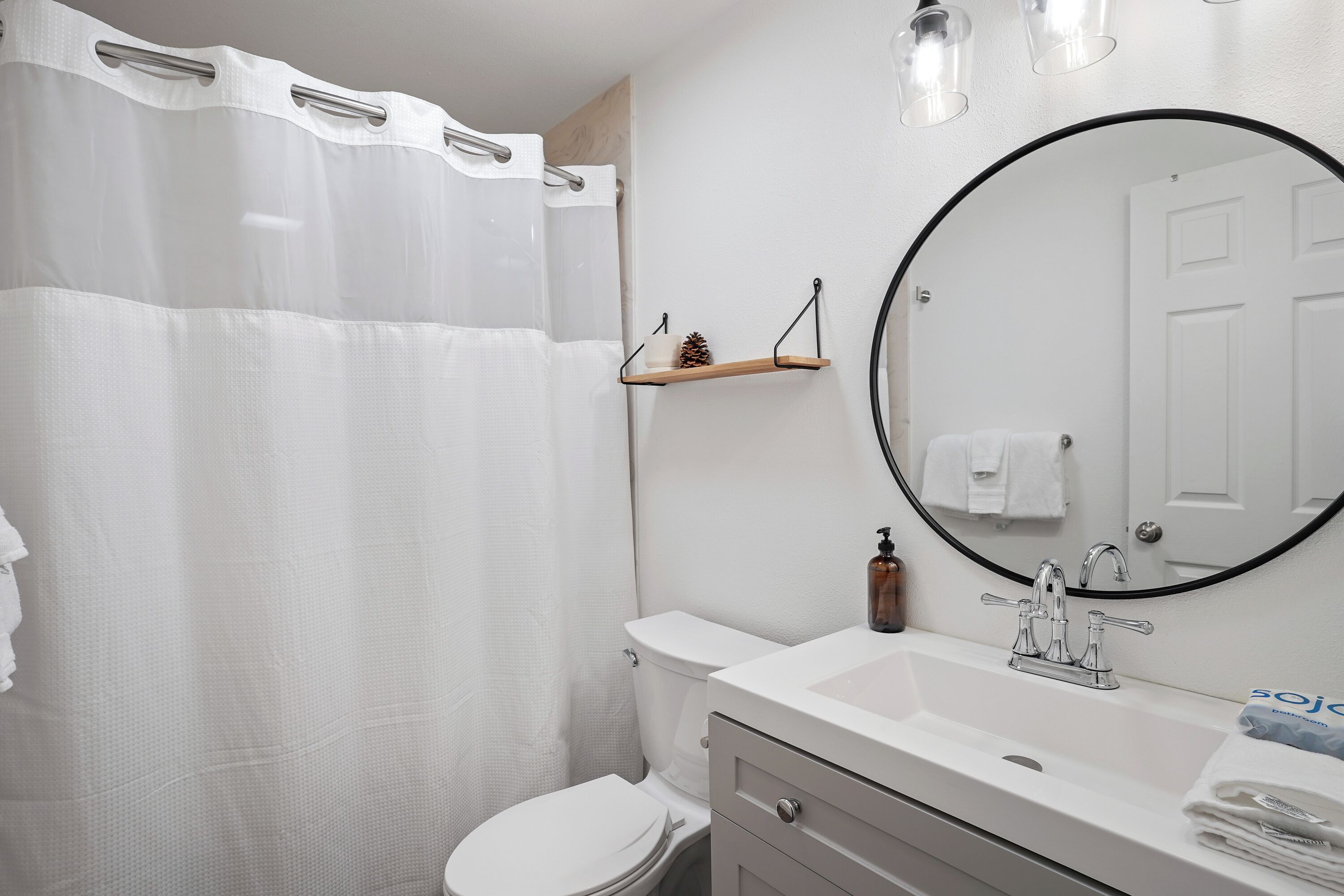 A bathroom with a white toilet, a white sink with a mirror above it, and a shower curtain.
