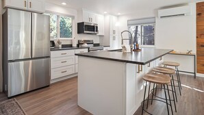 A modern kitchen with white cabinetry, stainless steel appliances, and a central island with bar stools. - Woodhaven House- 1-Acre Bend Oasis, Hot tub, w/office Studio, Pet-Friendly (Bend)