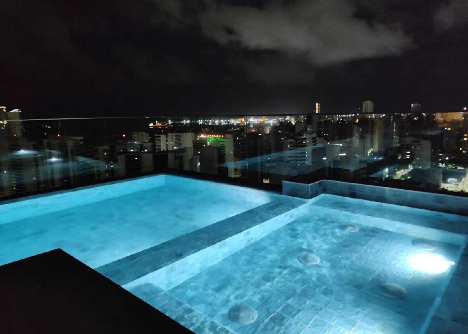 Une piscine sur le toit offrant une vue sur la ville illuminée la nuit.