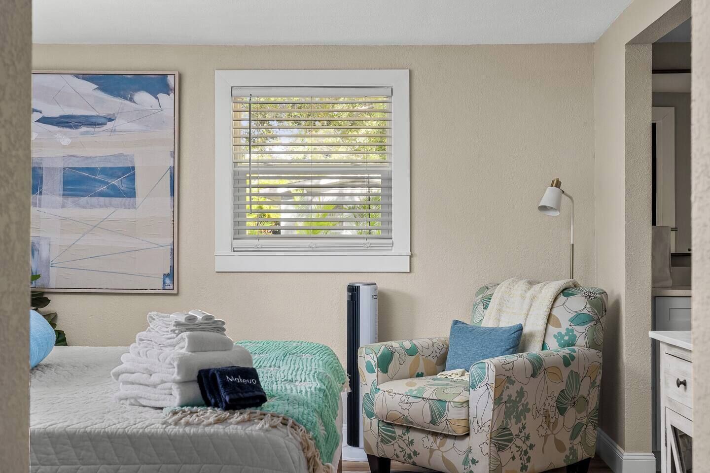 Une chambre à coucher avec un lit, une chaise, un radiateur, une fenêtre avec des stores et un tableau accroché au mur.