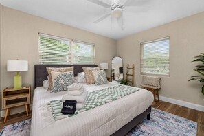 Un dormitorio con cama, mesita de noche, lámpara, espejo y ventilador de techo.