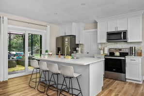Una cocina moderna con armarios blancos, una isla central con taburetes y un horno de acero inoxidable, además de un microondas sobre la estufa.