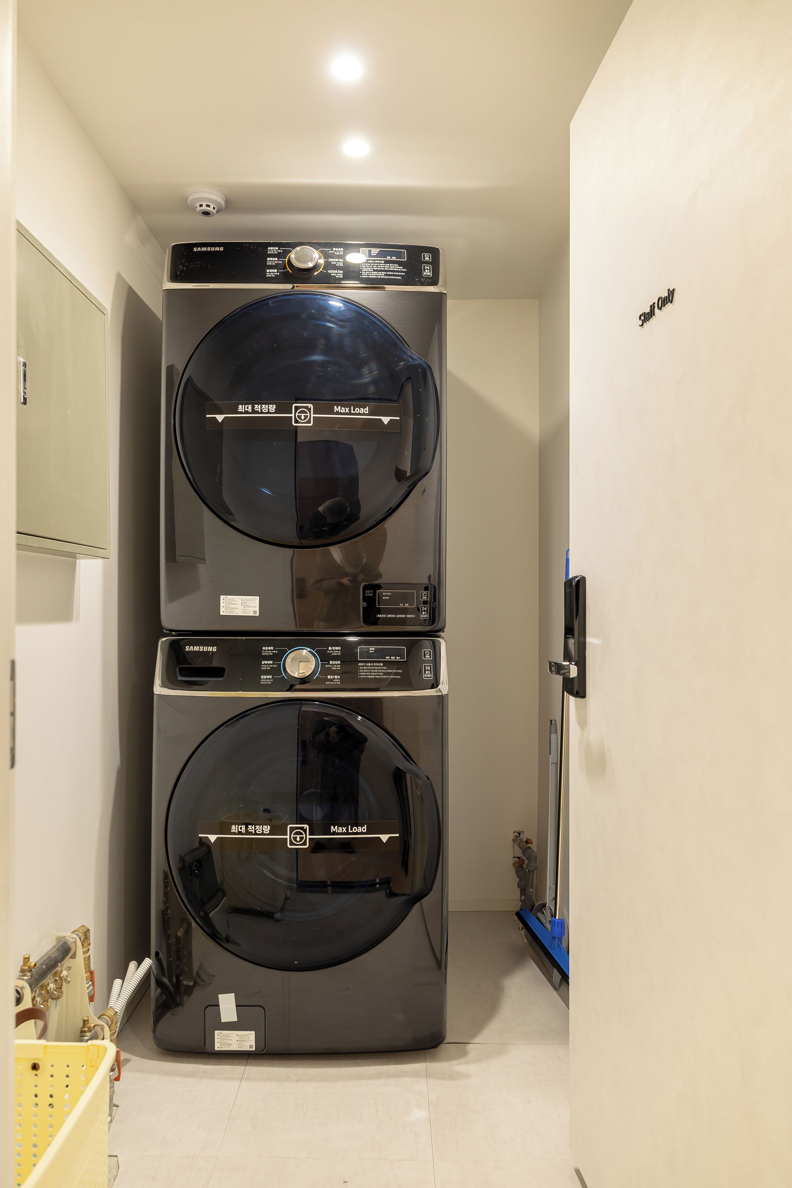 A laundry room with two stacked washing machines, a security camera, and a blue cleaning tool on the floor.