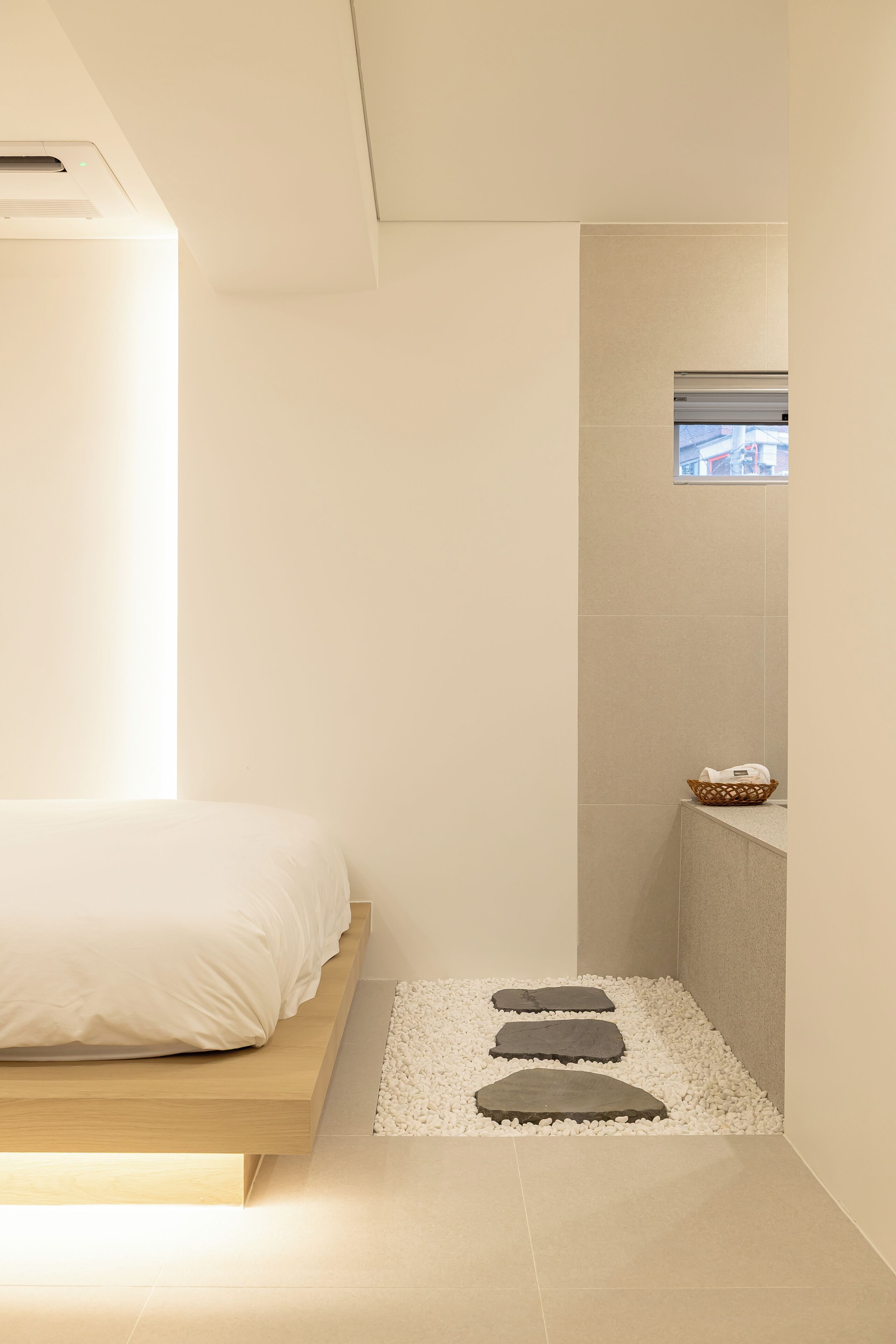Een moderne badkamer met een bed, een klein raam en een pad van steen dat naar een wastafel leidt.