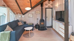A cozy cabin interior with a wooden ceiling, a sofa, a small table, a fireplace, and a television. - Gorgeous home in Ansager with WiFi (Ansager)
