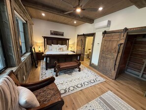 A spacious bedroom with a large bed, a wooden bench, a rustic ceiling, and a sliding barn-style door. - Yellowstone Adventure Lodge (Fremont County)