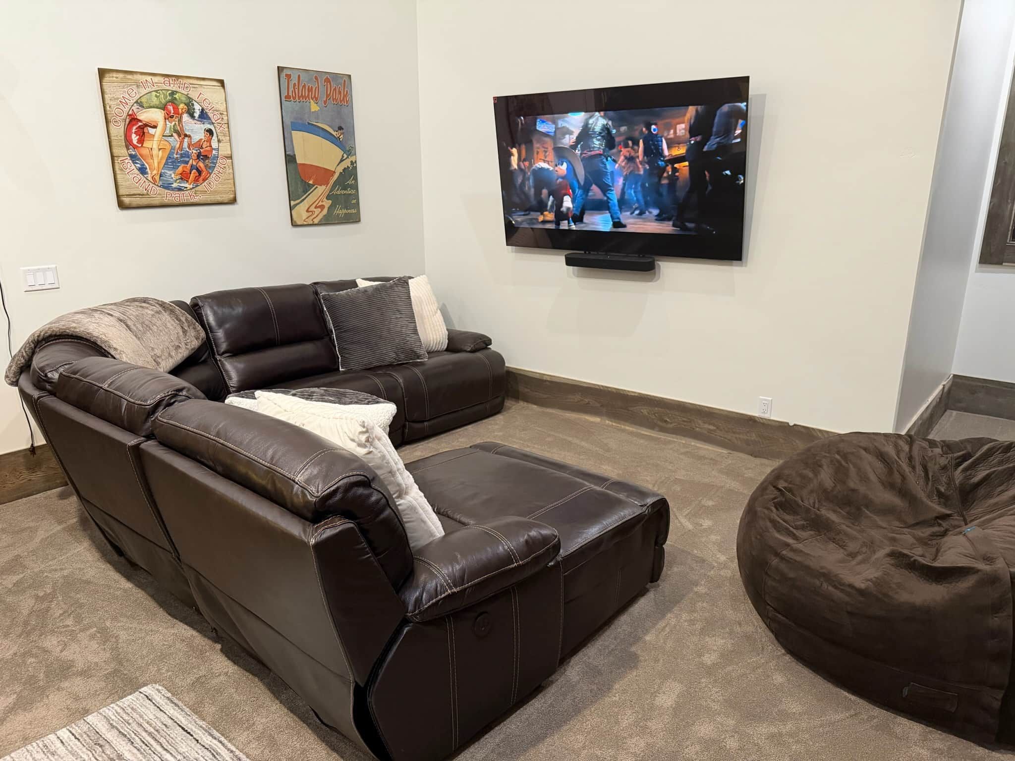 Een woonkamer met een leren bank, een aan de muur bevestigde televisie en een relaxfauteuil.