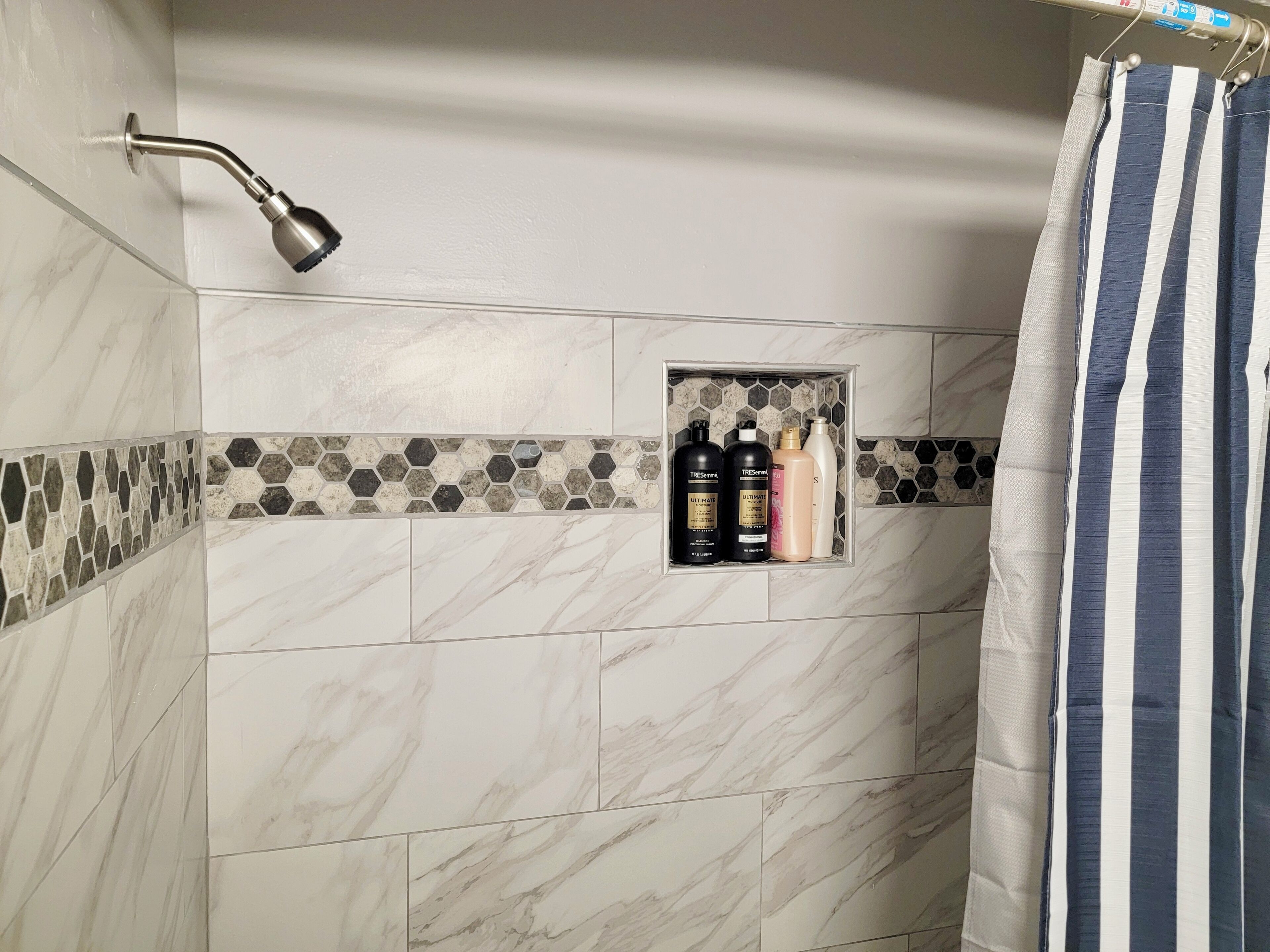 A bathroom with a shower, a towel rack, and a shelf with toiletries.