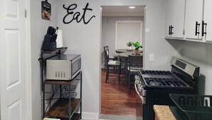 Una cucina con forno a microonde, piano cottura e pensili. Sul tavolo da pranzo c'è una pianta in vaso e un cartello a parete con scritto 'Eat'.