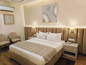 A hotel room with a bed, bedside tables, a lamp, a chair, and an air conditioning unit. - HOTEL PALLAVI GRAND (Panchkula)