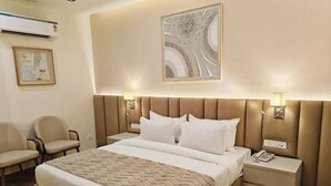 A hotel room with a large bed, two bedside tables, a chair, and a wall-mounted air conditioner. - HOTEL PALLAVI GRAND (Panchkula)