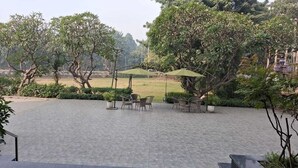 Un espace extérieur aménagé en terrasse, doté d’un sol carrelé, de plusieurs tables et chaises, et d’un grand parasol offrant de l’ombre.