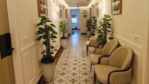 A hallway with patterned flooring, potted plants, and wall-mounted lamps. - HOTEL PALLAVI GRAND (Panchkula)