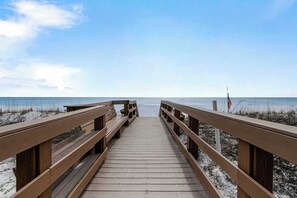 Ein Holzsteg führt zu einem Strand unter blauem Himmel.