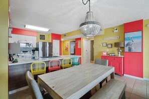 Une cuisine aux couleurs vives, avec un coin repas, agrémentée d’un lustre, de chaises colorées et d’une table en bois.