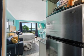 Una camera moderna con un letto, un divano, un angolo cottura con frigorifero e vista sull'esterno.