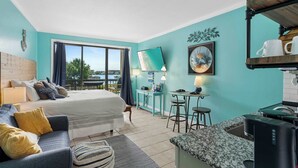 Une chambre d’hôtel moderne dotée d’un grand lit, d’un canapé, d’un coin cuisine et offrant une vue sur la mer.