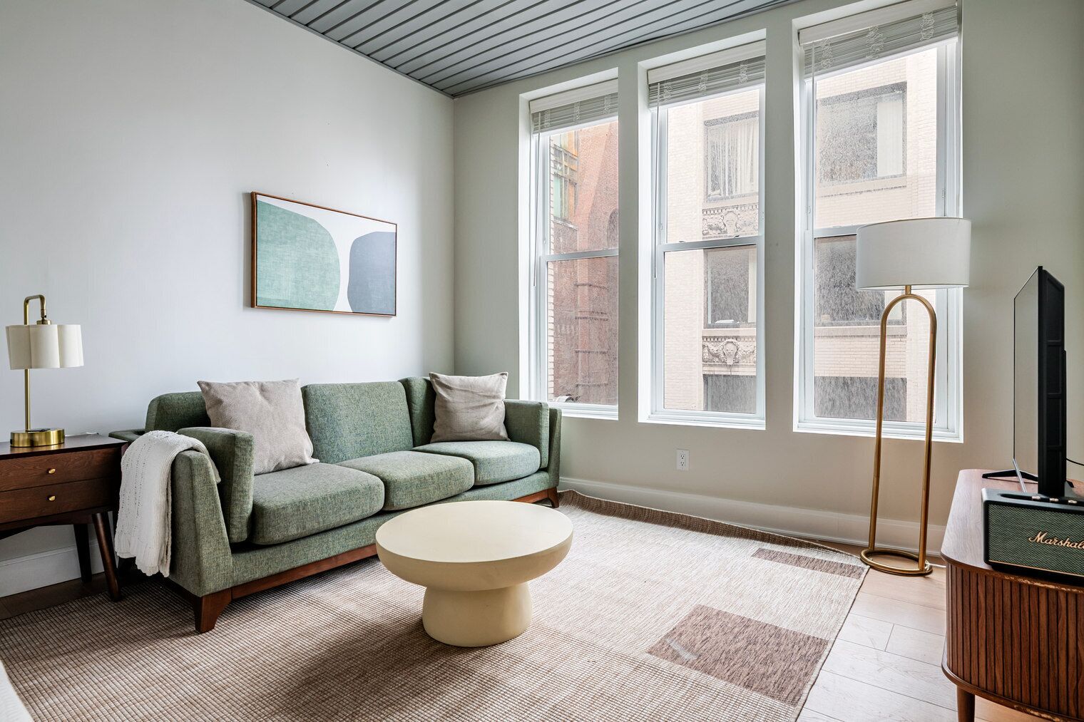 A living room with a green sofa, a round coffee table, a lamp, and a television on a wooden stand.